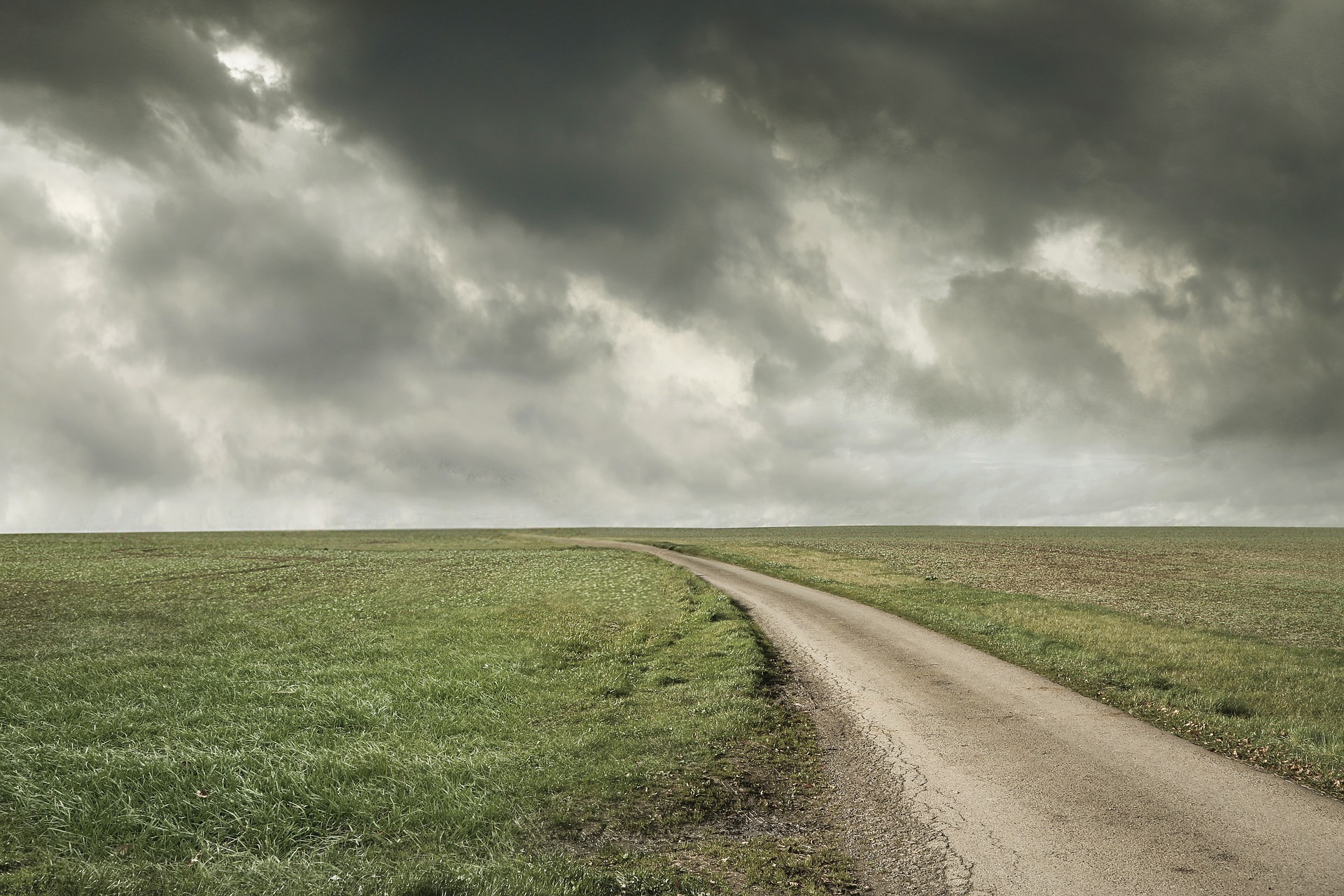 road through a pasture with storm clouds in the sky